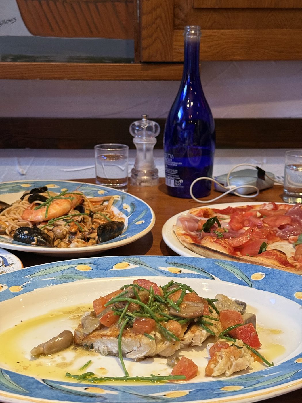 Grilled fish with tomatoes, with pizza and other dishes behind
