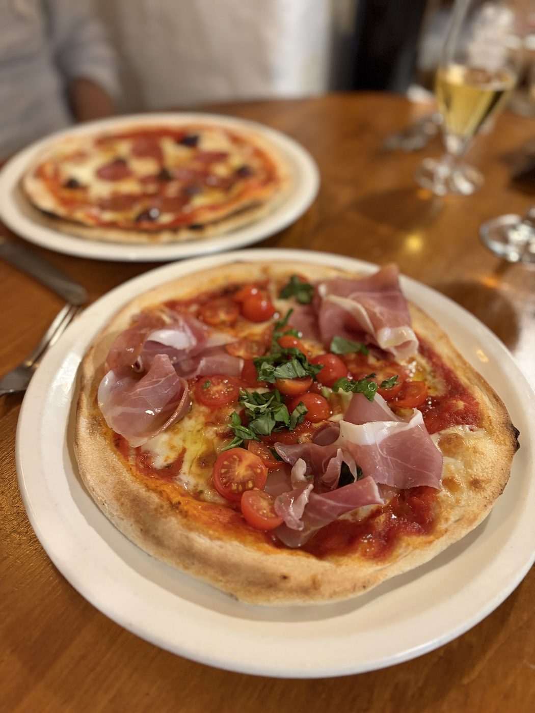 A prosciutto pizza with a margherita behind