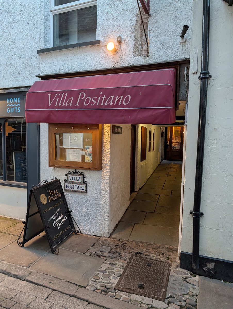 The white-painted front with the maroon Villa Positano awning and an A-board
